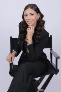 A girl sits in a chair. She wears a black suit.