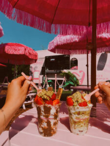 Two dessert cups sit on a table in front of the El Postrecito Food trailer.